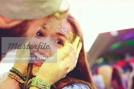 Portrait of young woman and boyfriend cupping her face with yellow chalked hand at festival