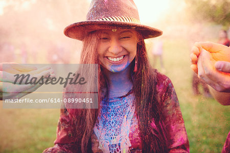 Hands covering young boho woman with coloured chalk powder at festival