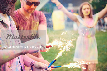 Young men covered in coloured chalk powder holding sparklers at festival