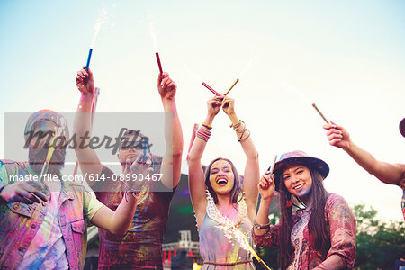 Young adults covered in coloured chalk powder dancing with sparklers at festival