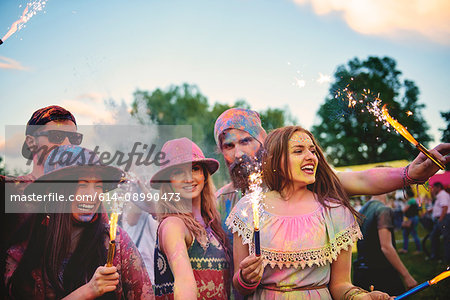 Young adults covered in coloured chalk powder dancing with sparklers at festival