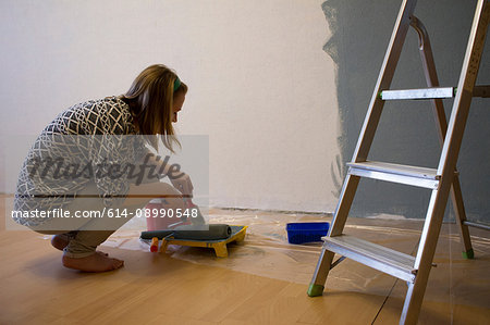 Young woman crouching to prepare grey paint for interior wall at home