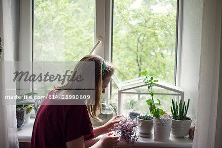 Young woman tending potted plants on windowsill