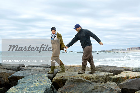 Young sea fishing couple stepping over beach rocks