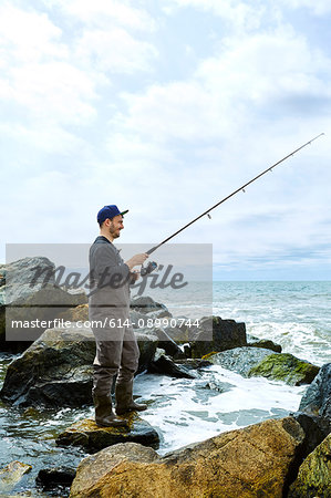 Young man standing on rock sea fishing