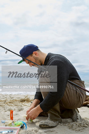 Crouching young man preparing fishing hook on beach