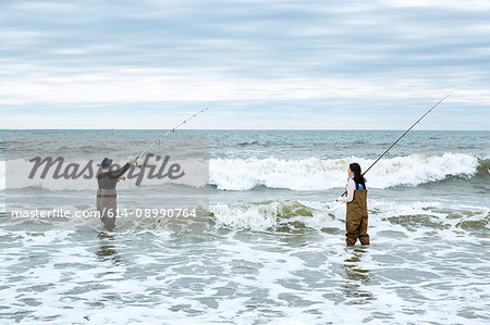 Young couple in waders, casting off sea fishing rods in sea
