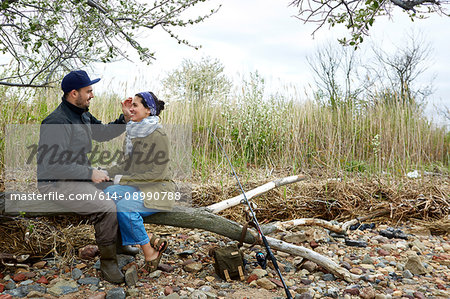 Romantic young couple sitting on tree trunk holding hands at beach