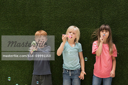 Children in front of artificial grass wall blowing bubbles