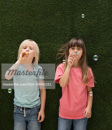 Children in front of artificial grass wall blowing bubbles
