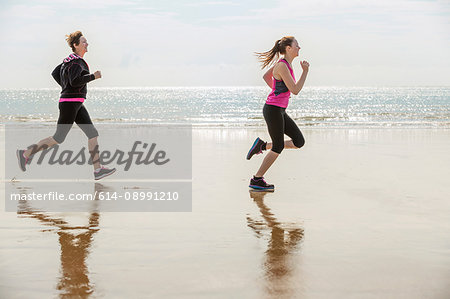 Mother and daughter running on beach, Folkestone, UK