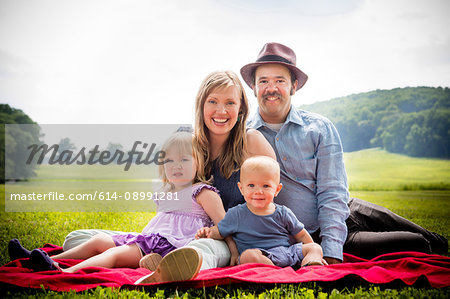 Portrait of mid adult couple sitting on picnic blanket with daughter and baby son