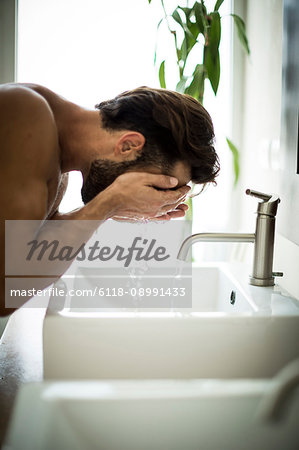 A man standing at a sink washing his face.