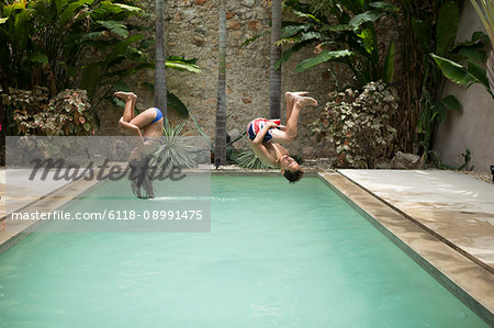 Two children in mid air, somersaulting backwards into a swimming pool.