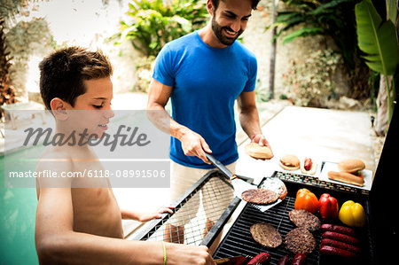 A man and boy standing at a barbecue cooking food.