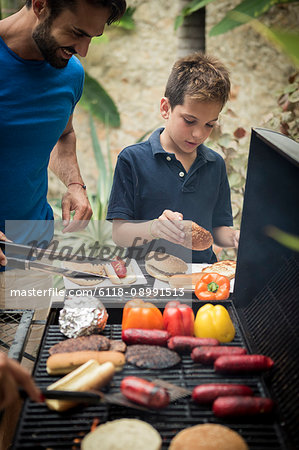 A man and boy standing at a barbecue cooking food.