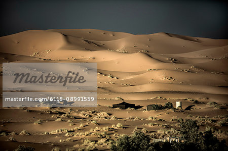 Desert landscape with sand dunes, tents in the middle distance.