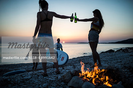 A group of young people gathered on a beach by a campfire.