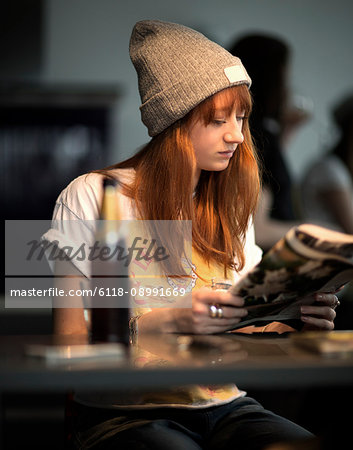 A young woman sitting at a table reading a newspaper.