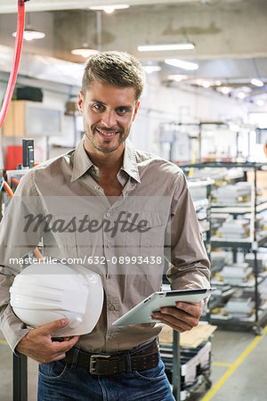 Factory worker holding hard hat and digital tablet, portrait