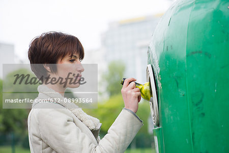 Woman putting wine bottle into recycling bin