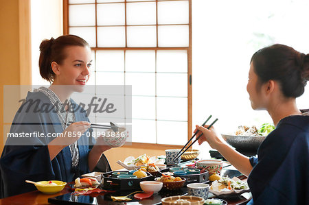 Caucasian woman wearing yukata eating with Japanese friend at traditional ryokan, Tokyo, Japan