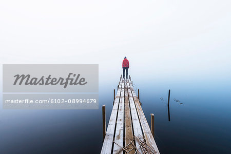 Man standing at the end of wooden pier Man standing at the end of wooden pier