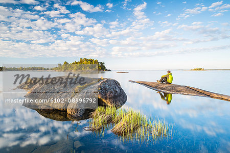 Man sitting on rock by lake on sunny day