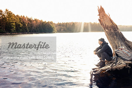 Man sitting on boulder by still lake