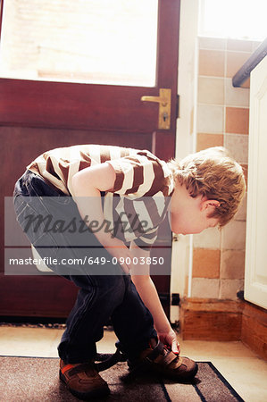 Boy tying his shoes at door