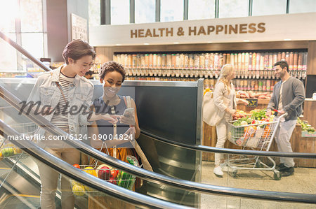 Young lesbian couple using cell phone on escalator in grocery store market
