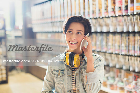 Smiling young woman with headphones talking on cell phone in grocery store market