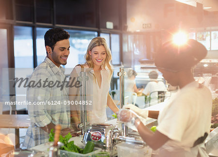 Female worker helping young couple at deli counter in grocery store market