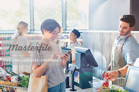 Young woman using cell phone at grocery store market checkout