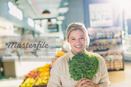 Portrait smiling young woman holding bunch of kale in grocery store market