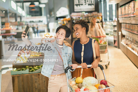 Smiling young lesbian couple taking selfie in grocery store market