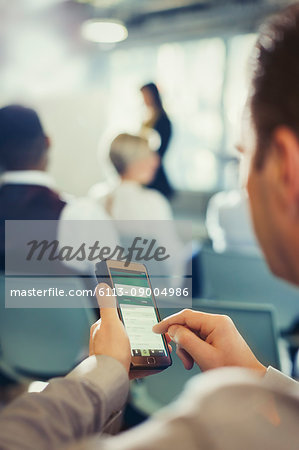 Businessman texting with cell phone in conference audience