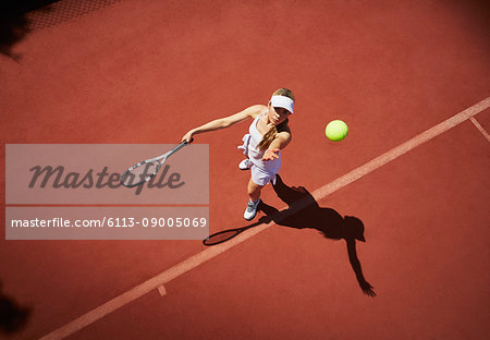 Overhead view young female tennis player playing tennis, serving the ball on sunny clay tennis court