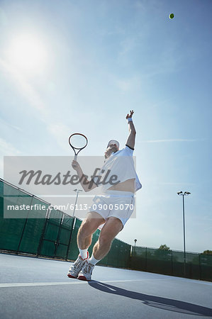 Young male tennis player playing tennis, serving the ball on sunny tennis court