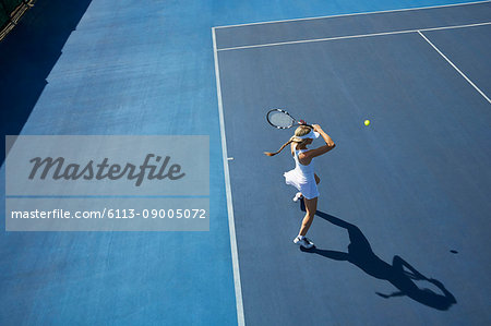 Overhead view young female tennis player playing tennis on sunny blue tennis court