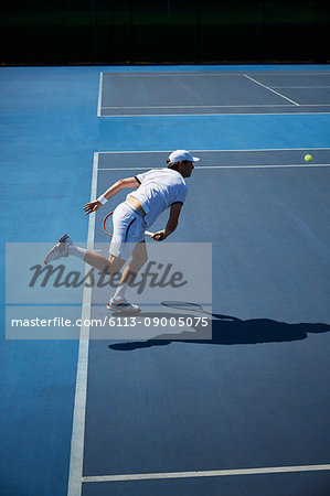 Male tennis player playing tennis on sunny blue tennis court