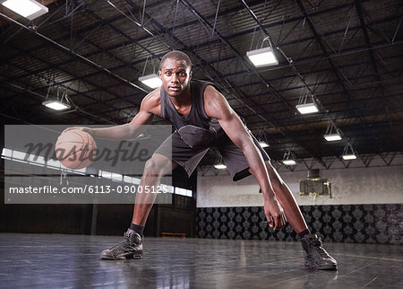 Portrait confident young male basketball player dribbling the ball on court in gymnasium