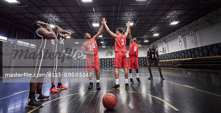 Young male basketball players high-fiving, celebrating on court in gymnasium