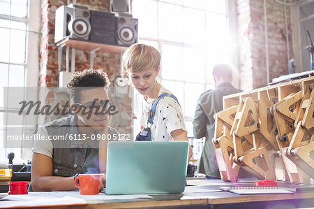Serious, focused designers working at laptop in workshop