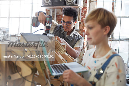 Designers using laptop and power drill in workshop