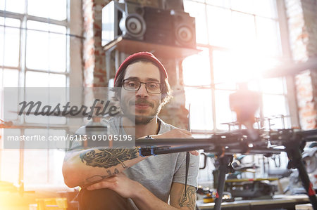 Portrait confident male designer with tattoos working on drone in workshop