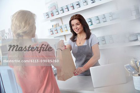 Female business owner giving shopping bag to shopper in art paint shop