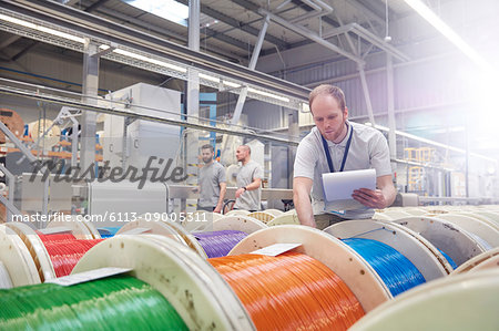 Male worker with clipboard checking multicolor spools in fiber optics factory