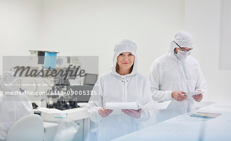 Portrait smiling female engineer in protective suit with paperwork in fiber optics research and testing laboratory