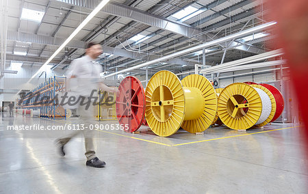 Male worker walking by large spools in fiber optics factory